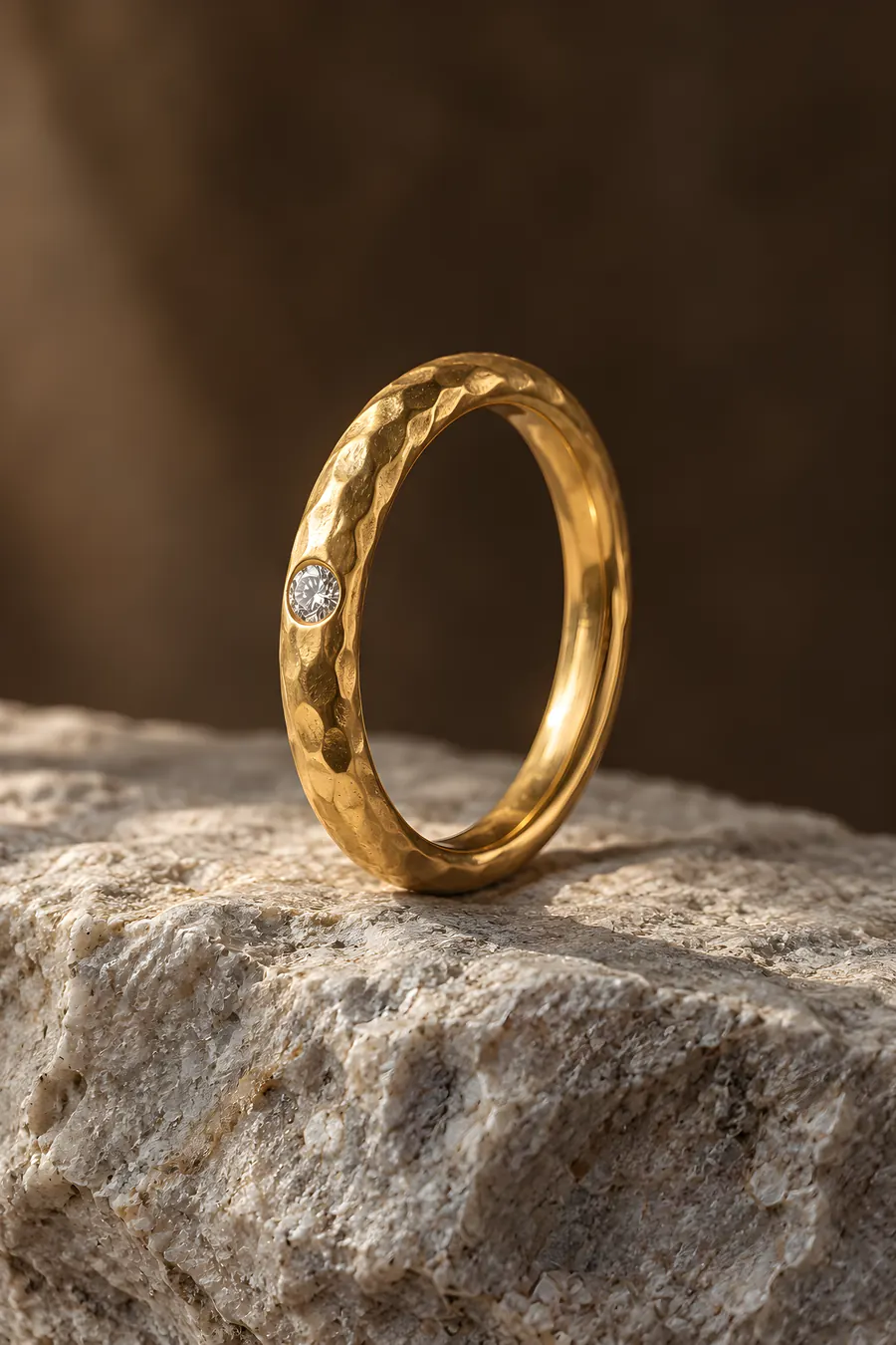 Gehämmerter Goldring mit einem kleinen eingelassenen Brillanten auf einem hellen Stein