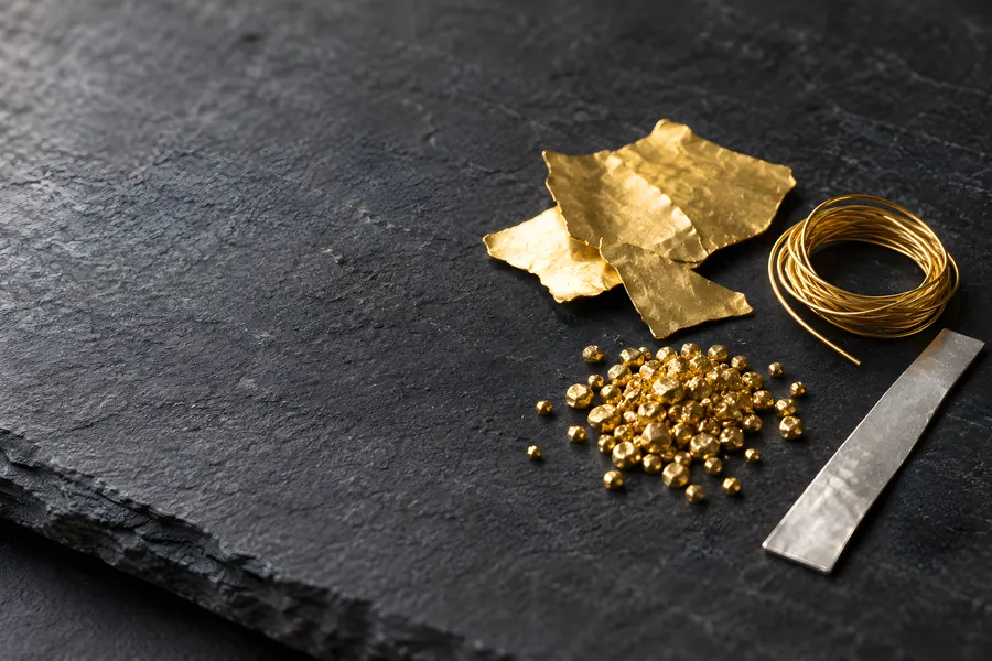 Goldblech-Abschnitte, ein Ring aus Golddraht, Granalien und ein Silberstreifen auf Schiefer